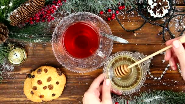 Té de invierno Una taza de té con miel y croissant o galletas, una rama de un árbol de Navidad en la nieve, luces de Navidad — Vídeos de Stock