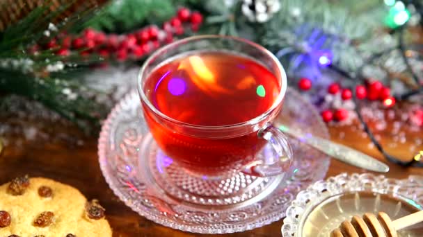 Té de invierno Una taza de té con miel y croissant o galletas, una rama de un árbol de Navidad en la nieve, luces de Navidad — Vídeo de stock