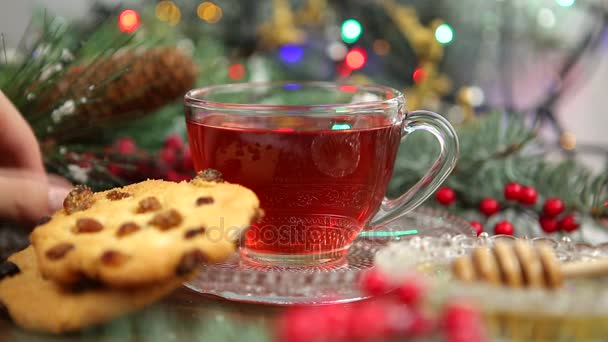 En kopp te med honung och cookies, en gren av en julgran i snön, julbelysning — Stockvideo