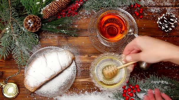 Té de invierno Una taza de té con miel y croissant o galletas, una rama de un árbol de Navidad en la nieve, luces de Navidad — Vídeos de Stock