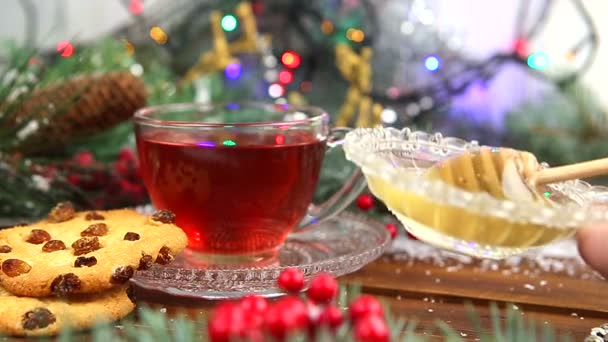 Una taza de té con miel y galletas, una rama de un árbol de Navidad en la nieve, luces de Navidad — Vídeo de stock
