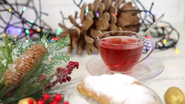 Una taza de té con miel y croissant, una rama de un árbol de Navidad en la nieve, luces de Navidad — Vídeos de Stock