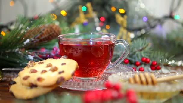 Eine Tasse Tee mit Honig und Keksen, ein Zweig eines Weihnachtsbaums im Schnee, Weihnachtsbeleuchtung — Stockvideo