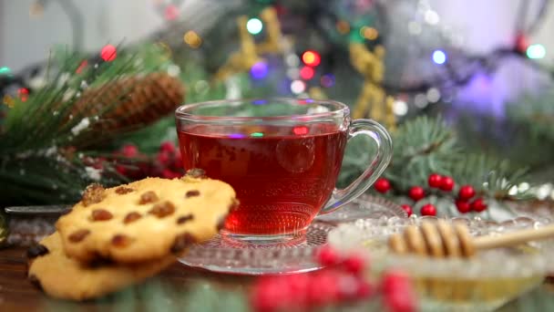Eine Tasse Tee mit Honig und Keksen, ein Zweig eines Weihnachtsbaums im Schnee, Weihnachtsbeleuchtung — Stockvideo