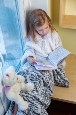 Şirin bir bebek odasında kışın pencerenin önünde oturur ve bir kitap okur