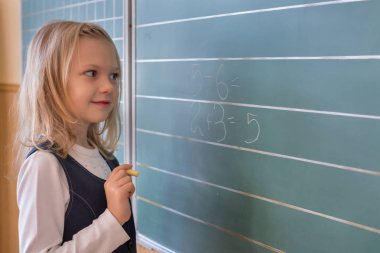 İlk sınıf öğrencisi bir kız okul ders yeşil tahtaya yazma