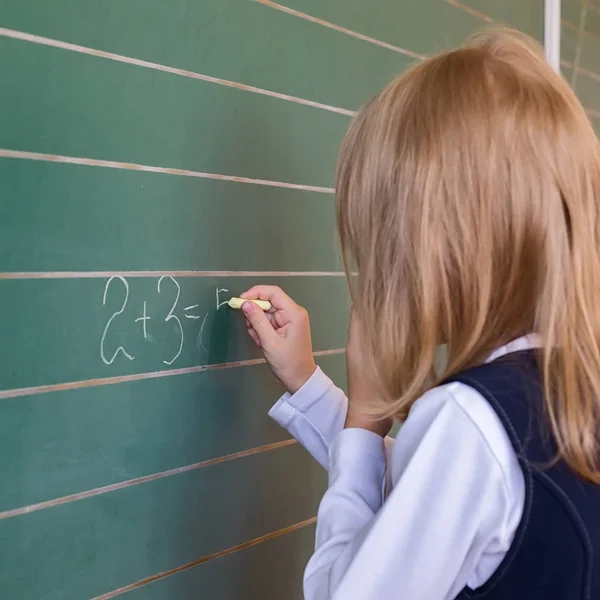 Aluno da primeira série uma menina escrevendo em quadro-negro verde na lição da escola — Fotografia de Stock
