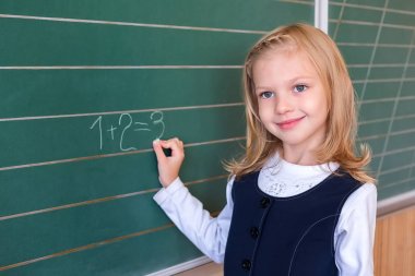 İlk sınıf öğrencisi bir kız okul ders yeşil tahtaya yazma