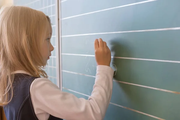 Pierwszej klasy Uczeń dziewczyna pisania na zielone tablicy w szkole lekcji — Zdjęcie stockowe