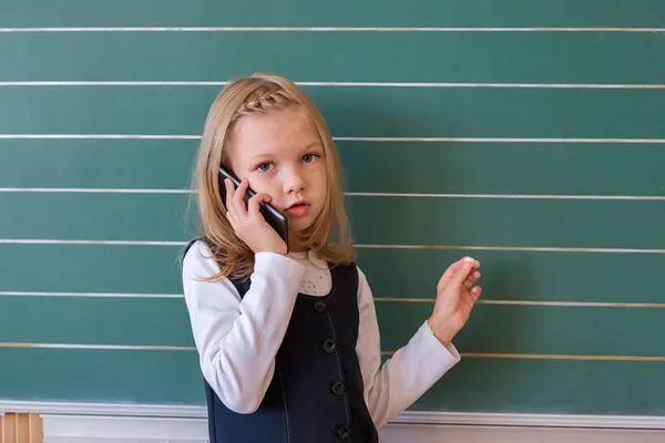 Bir ilk sınıf öğrencisi okulda telefonla konuşuyor. duygular kız öğrenciler — Stok fotoğraf
