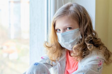 Oyuncak ayıyla maskeli bir kız, pencereden dışarı bakıyor, Coronavirus 'u karantinaya alıyor. hasta çocuklar