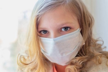 Oyuncak ayıyla maskeli bir kız, pencereden dışarı bakıyor, Coronavirus 'u karantinaya alıyor. hasta çocuklar