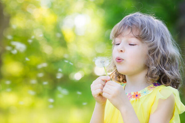 Happy child blowing dandelion flower outdoors