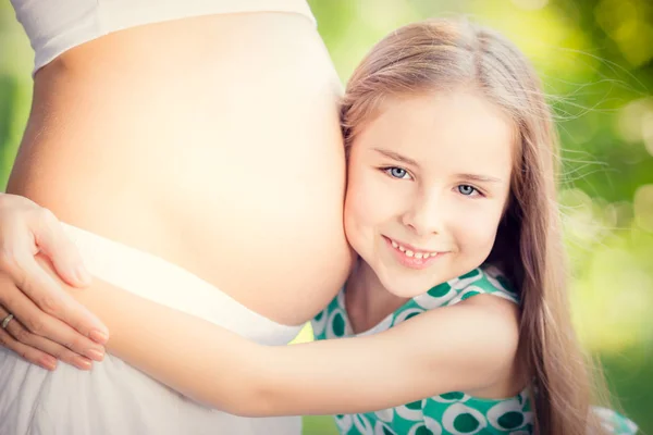 Счастливый ребенок с животом беременной женщины — стоковое фото