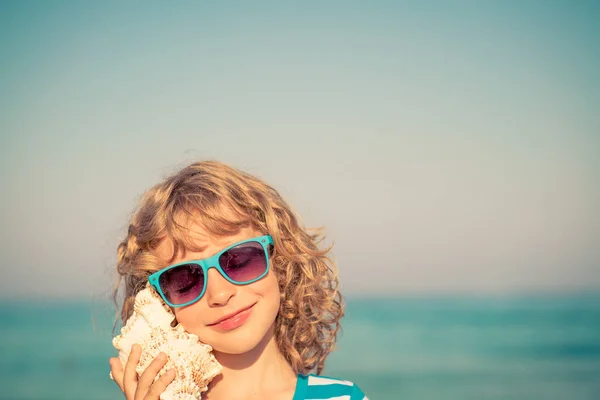 Boldog gyermek hallgatni seashell a strandon — Stock Fotó