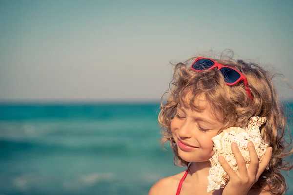 Gelukkig kind luisteren zeeschelp op het strand — Stockfoto