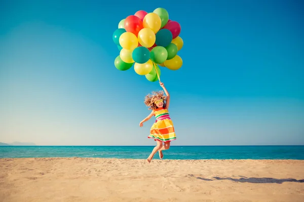 Criança feliz pulando com balões coloridos na praia — Fotografia de Stock