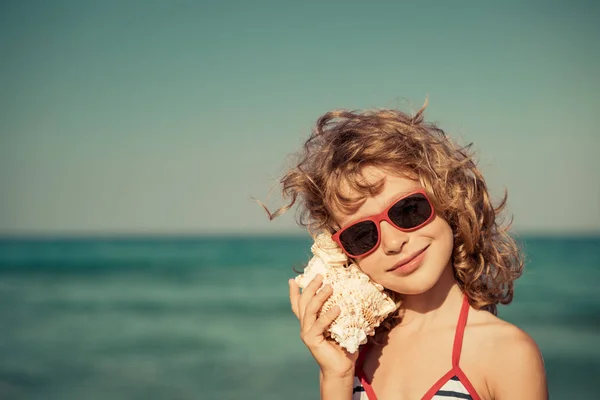 Felice bambino ascoltare conchiglia sulla spiaggia — Foto Stock