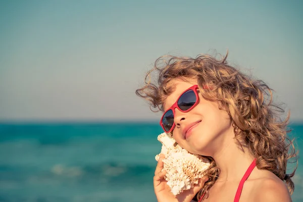 Glückliches Kind hört Muschel am Strand — Stockfoto