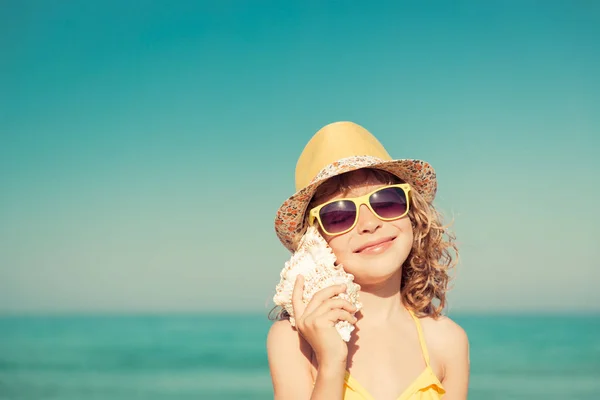 Criança feliz ouvir concha na praia — Fotografia de Stock