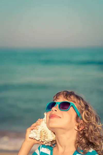 Ευτυχισμένο παιδί ακούει seashell στην παραλία — Φωτογραφία Αρχείου