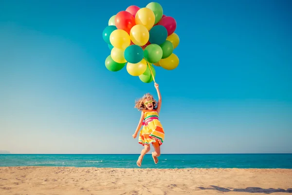 Gelukkig kind springen met kleurrijke ballonnen aan zandstrand — Stockfoto