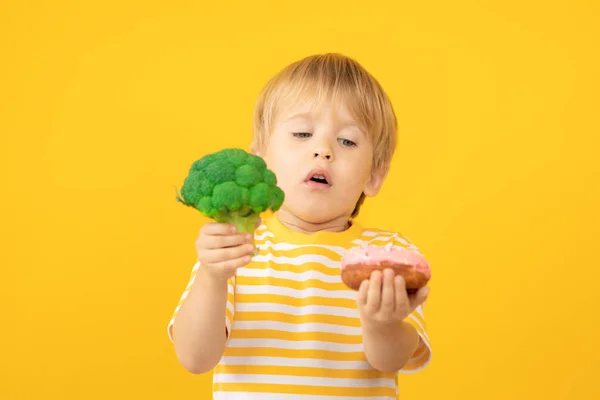 Criança feliz segurando donut e brócolis — Fotografia de Stock