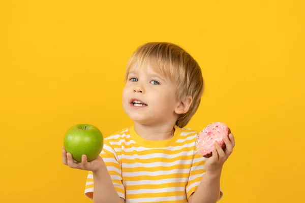 Niño feliz sosteniendo donut y manzana —  Fotos de Stock