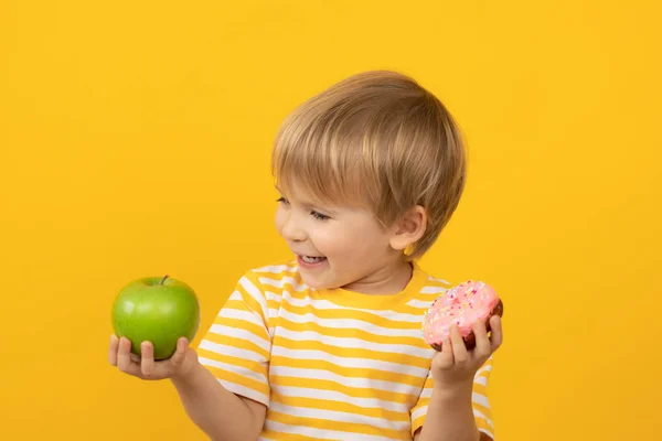 Счастливый ребенок держит пончик и яблоко — стоковое фото