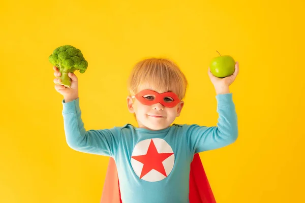 Superhjälte barn som håller broccoli och äpple — Stockfoto