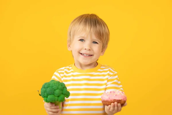 Criança feliz segurando donut e brócolis — Fotografia de Stock