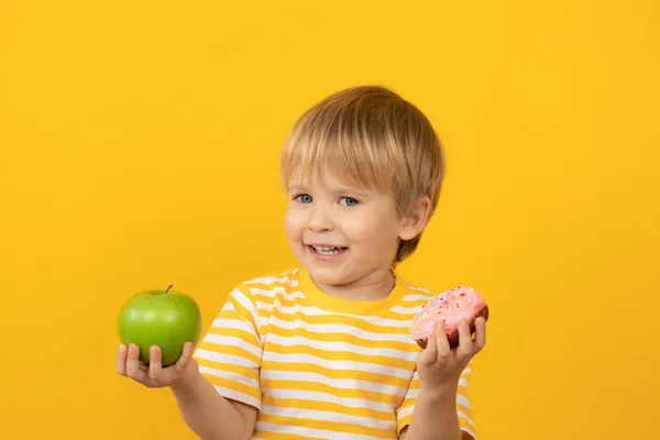 Criança feliz segurando donut e maçã — Fotografia de Stock