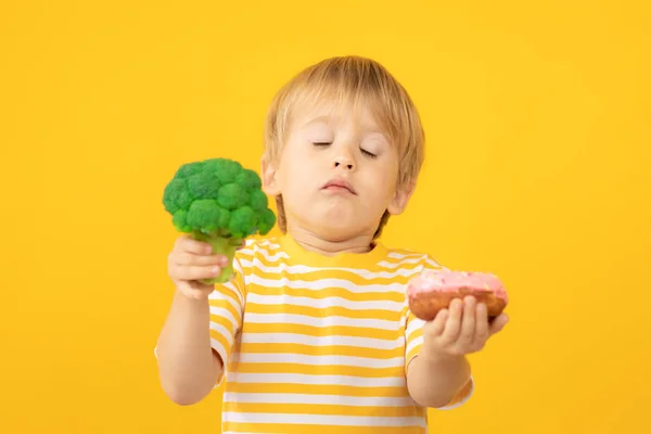 Niño feliz sosteniendo donut y brócoli —  Fotos de Stock