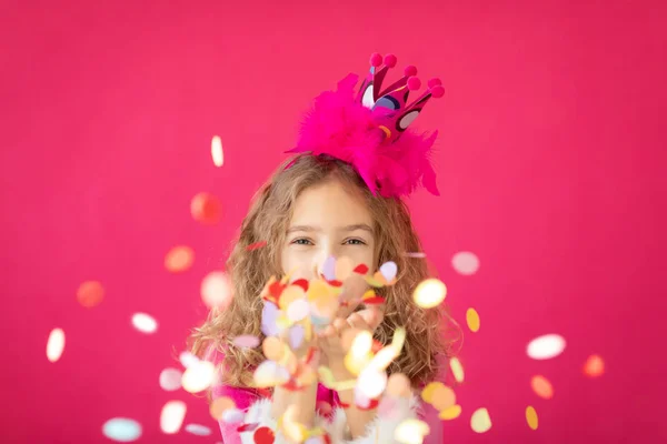 Menina fantasia soprando confete contra o chão de padaria rosa — Fotografia de Stock