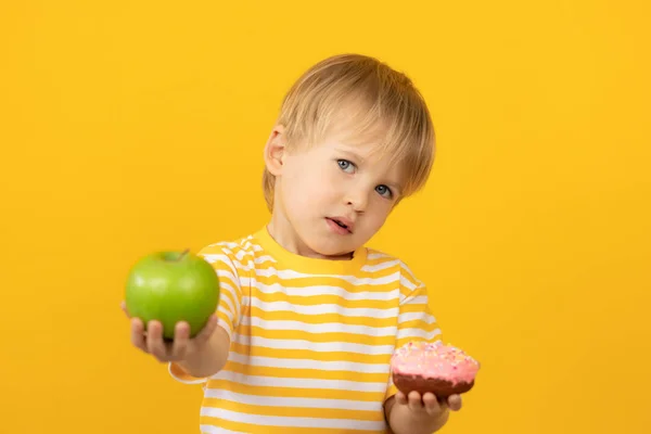 Šťastné dítě drží koblihu a jablko — Stock fotografie