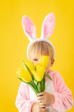 Funny kid wearing Easter bunny against yellow background