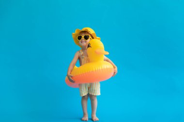 Mavi arka planda sarı plastik ördekli mutlu çocuk portresi. Çocuk yaz tatilinde eğleniyor. Rüya ve hayal gücü kavramı