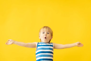 Sarı arka planda mutlu çocuk portresi. Çocuk yaz tatilinde eğleniyor. Rüya ve hayal gücü kavramı