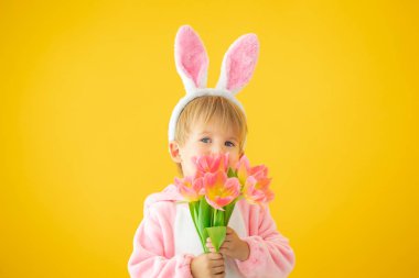 Sarı arka planda Paskalya tavşanı takan komik çocuk. Bir buket çiçek tutan mutlu çocuk. Bahar tatili kavramı