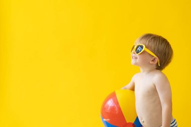Sarı arka planda plaj topu tutan mutlu çocuk portresi. Çocuk yaz tatilinde eğleniyor. Rüya ve hayal gücü kavramı