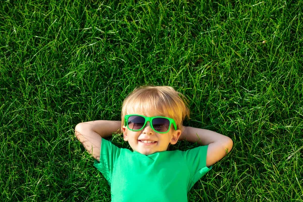 幸せな子供の緑の草の上に横たわる 春の庭で楽しい屋外を持っている笑顔の男の子 — ストック写真