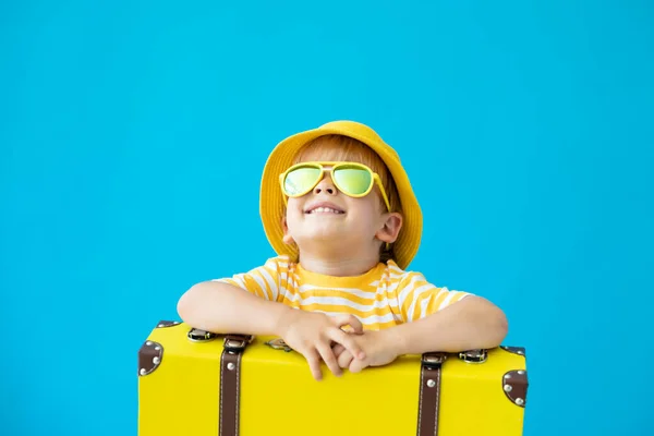 青い背景に黄色のスーツケースと幸せな子供の肖像画 夏休みを楽しんでいる子供 夢と想像力の概念 — ストック写真
