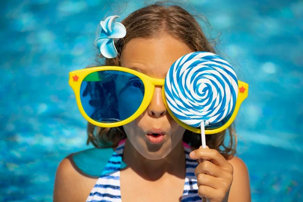 プールでロリポップと驚きの子供 女の子持っています楽しいです夏休みに青水の背景に対して — ストック写真