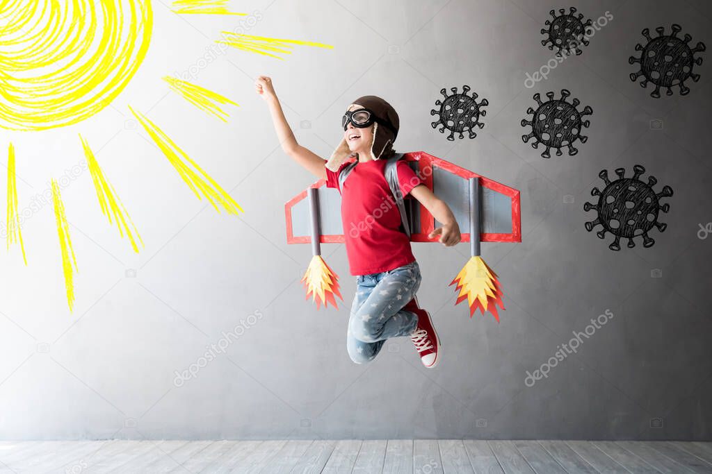 Happy child jumping with toy cardboard wings. Kid pilot flying away from covid virus. Sun and vitamin D concept