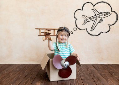 Mutlu çocuk pilot olmayı hayal ediyor. Çocuk evde eğleniyor. Çizgili tişörtlü çocuk karton kutuda oynuyor. Yaz tatili ve seyahat konsepti. Hayal ve hayal gücü