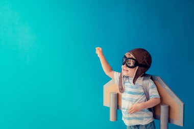 Mutlu çocuk mavi arka planda oyuncak kağıdıyla oynuyor. Çocuk evde eğleniyor. Hayal gücü, yaratıcı ve başlangıç konsepti