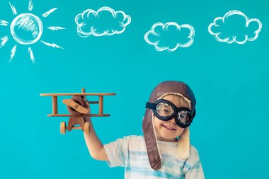 Mutlu çocuk klasik ahşap uçakla oynuyor. Çocuk mavi arka planda eğleniyor. Hayal gücü ve özgürlük kavramı