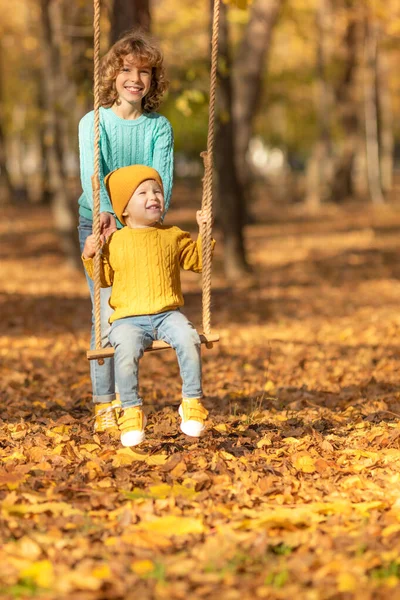 快乐的孩子们在秋天的公园里玩得很开心 孩子们在黄色模糊的树叶背景下荡秋千 自由和无忧无虑的概念 — 图库照片