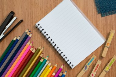 Boş defter, renkli pensils ve Danışma çalışmaları hakkında herhangi bir fikir için ahşap masa üzerinde zımba.