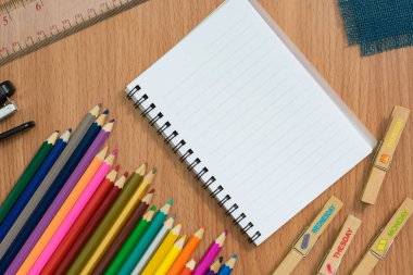 Boş defter, renkli pensils ve Danışma çalışmaları hakkında herhangi bir fikir için ahşap masa üzerinde zımba.